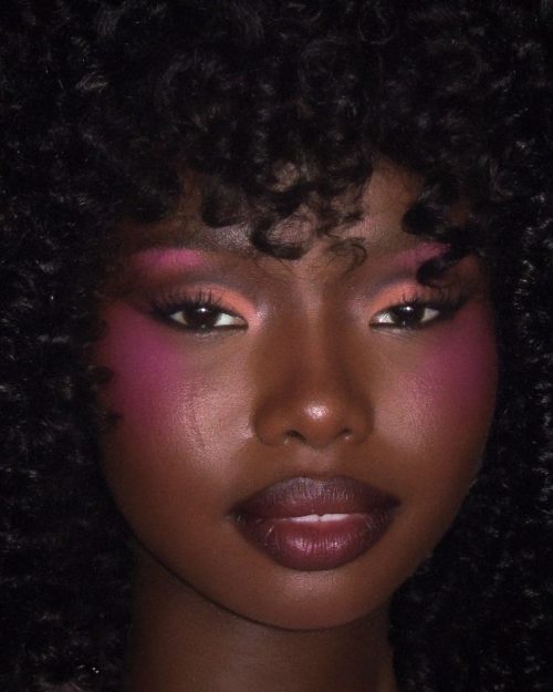 Black woman with make up. Bright Pink Blush appled underneath the eyes and on the apples of the cheek to emulate a baby doll look